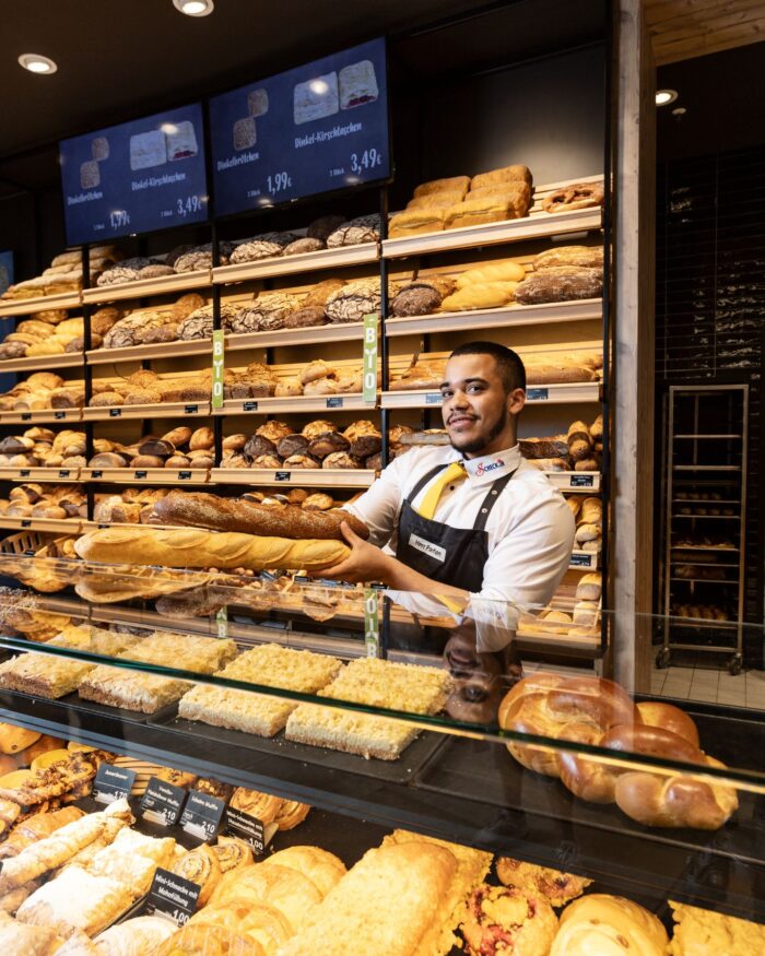 Mitarbeiter steht an Theke mit Brötchen und Brot